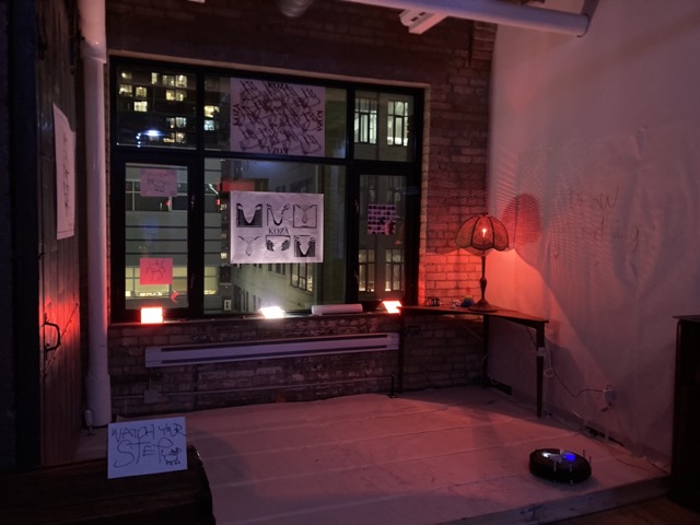 A room at night with artwork placed on the window facing other buildings. 